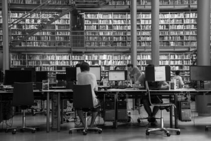 A black and white photo of people working at computers in a library.
